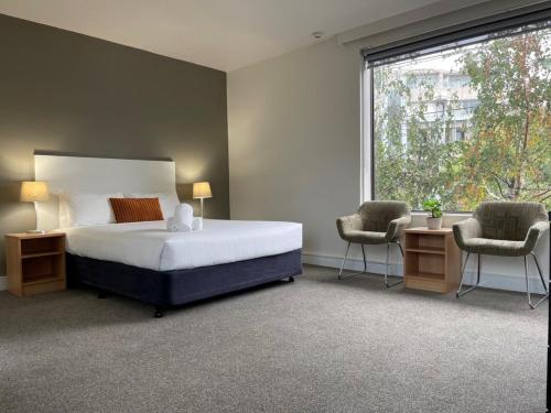 a bedroom with a bed and two chairs and a window at Cosmopolitan Hotel and Apartments in Melbourne