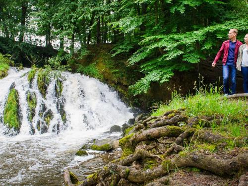 two people standing in front of a waterfall at Domaine de Blangy in Hirson