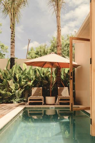 two chairs and an umbrella next to a swimming pool at NORI Boutique Villas Uluwatu - Breakfast Available in Uluwatu