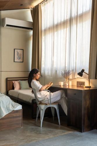 a woman sitting at a desk in a bedroom at Cove by Raho - Nestled Away Retreat in Siddapur