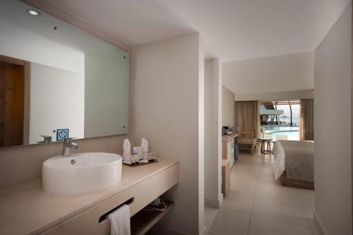 ein Badezimmer mit Waschbecken und Spiegel und ein Schlafzimmer in der Unterkunft Select Sosua Adults Only, Trademark by Wyndham All Inclusive in Sosúa