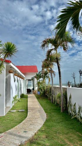 a walkway next to a white building with palm trees at Beach Villas Phan Thiêt in Bình Sum