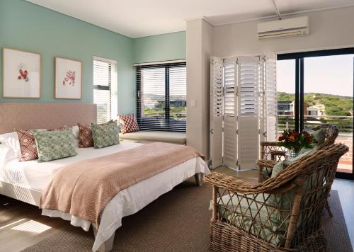 a bedroom with a bed and a chair and windows at Christiana Lodge in Plettenberg Bay