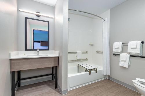 a bathroom with a sink and a tub and a mirror at ECHO Suites Extended Stay by Wyndham Dallas Plano Richardson in Plano