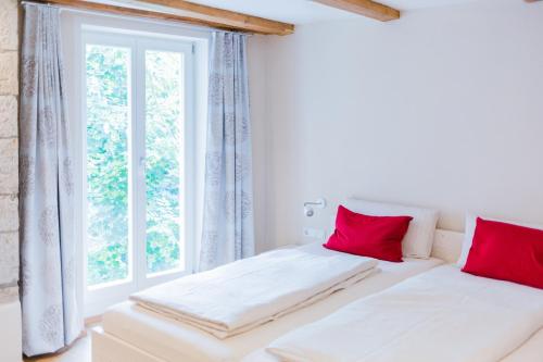 a white bedroom with red pillows and a window at Hellbachhof in Equarhofen