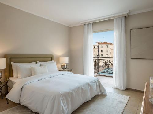 a bedroom with a white bed and a large window at Grecotel Larissa Imperial in Larisa