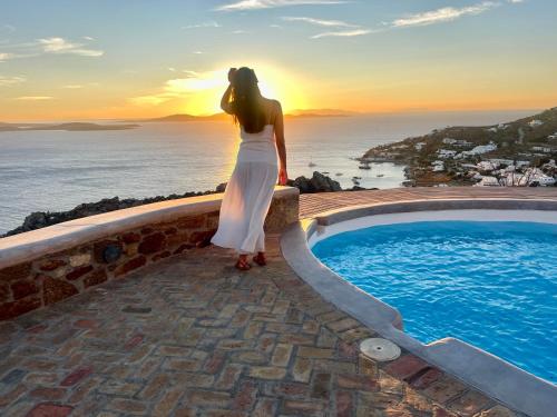 a woman standing next to a swimming pool at sunset at Villa Tavani Agios Ioannis Mykonos in Agios Ioannis Mykonos