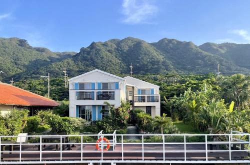 a white house with mountains in the background at Vacances a la mer Ishigaki in Ishigaki Island