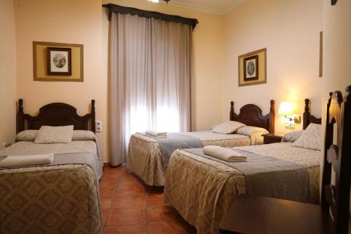 ein Hotelzimmer mit drei Betten und einem Fenster in der Unterkunft Hostal Rocio in Sanlúcar la Mayor