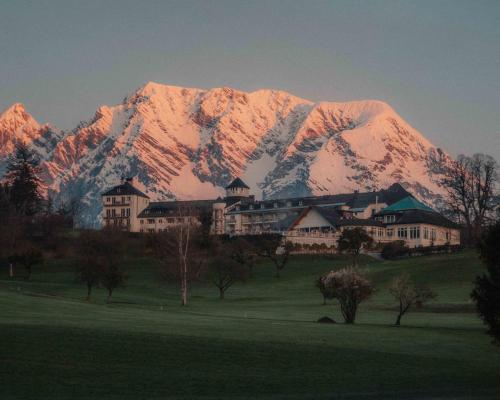 a building in front of a mountain with a house at IMLAUER Hotel Schloss Pichlarn in Aigen im Ennstal