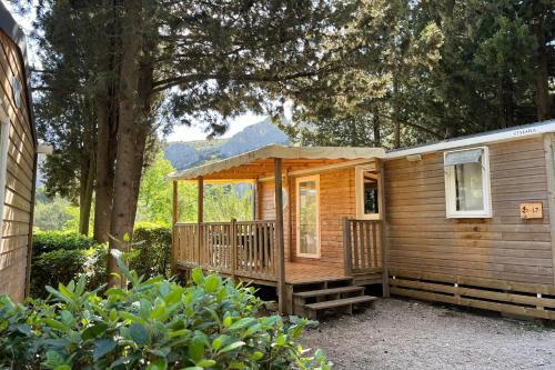 a wooden cabin with a porch and a large tree at Camping de la Vallée Heureuse in Orgon