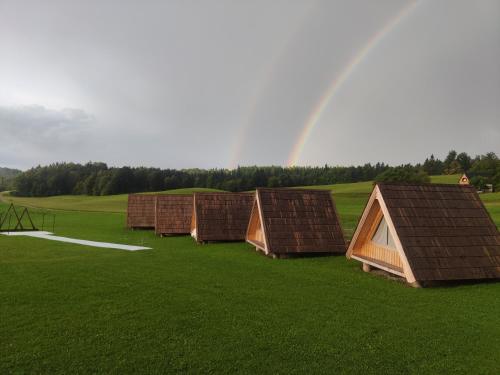 a row of huts in a field with a rainbow in the background at Glamp Pr Kuzuc in Cerklje na Gorenjskem