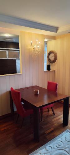 a dining room table with red chairs and a clock at Apartament Rycerska LUX in Łomża
