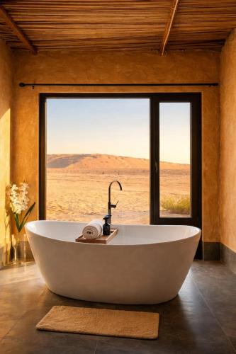 a bath tub in a room with a large window at Desert Wonders Camp in Ḩawīyah
