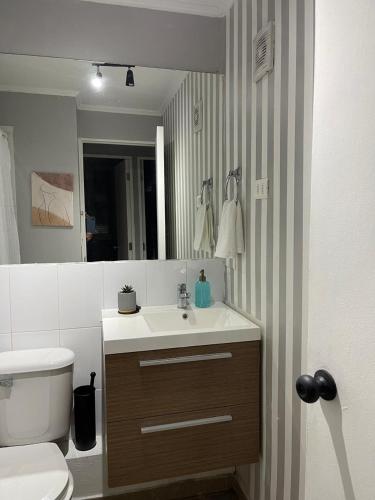 a bathroom with a sink and a toilet and a mirror at Departamento outlet Puerto Montt con estacionamiento in Puerto Montt