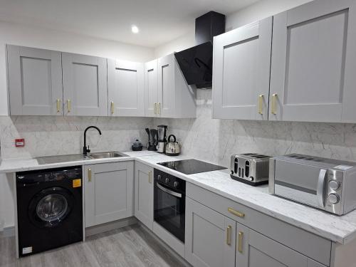 a kitchen with white cabinets and a sink and a microwave at New & Lovely Spacious 2-Bedroom Villa in Coventry