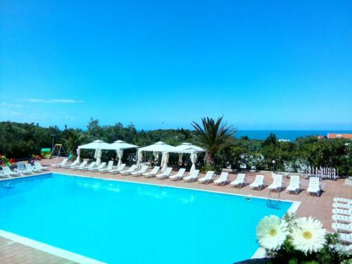 a swimming pool with chairs and umbrellas and the ocean at Hotel Club Bellavista in Vieste