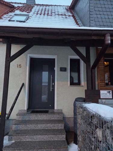 a house with a black door and stairs in the snow at Ferienwohnung Salza in Nordhausen