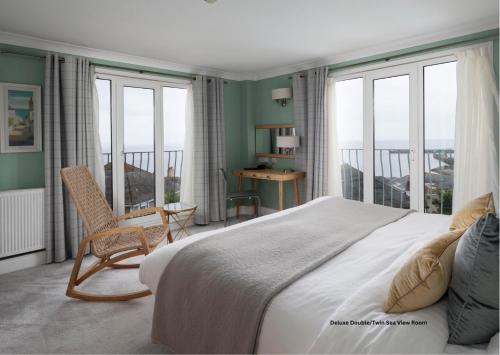 a bedroom with a large bed with a chair and windows at Hotel Penzance Harbour View in Penzance