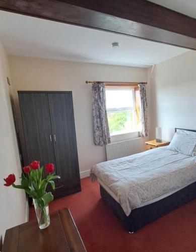 a bedroom with a bed and a vase of flowers on a table at Teach Hudi Beag, Bar & Accommodation Bunbeg in Bunbeg