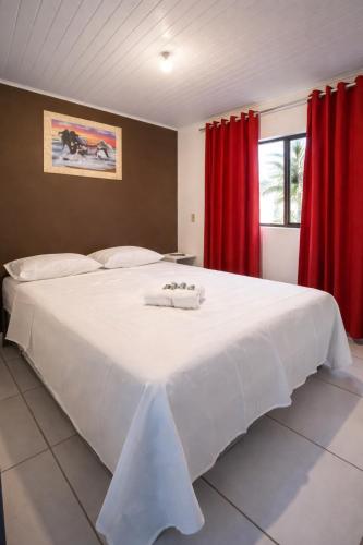 a bedroom with a large white bed with red curtains at Pousada da Heloisa in Imbituba