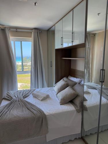a bedroom with a large white bed with a glass wall at Mandai Apart - Beira Mar in Cabo Frio