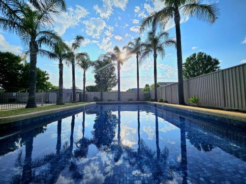 a swimming pool with palm trees and a fence at The Wyndhamere Motel Shepparton in Shepparton