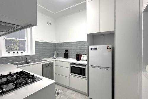 a white kitchen with a stove and a refrigerator at Level Access, 2 Mins Walk to Corso, Wharf, Harbour in Sydney