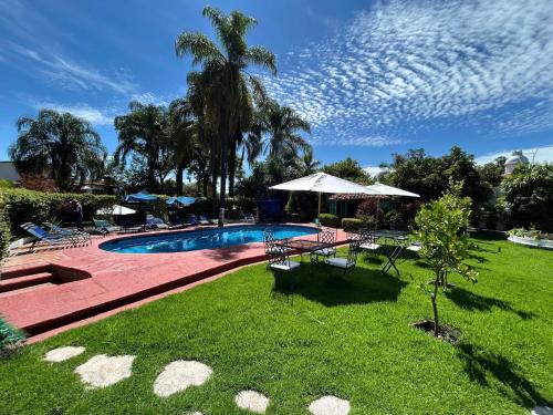 a yard with a swimming pool with chairs and an umbrella at Posada Los Alcatraces in Atlixco