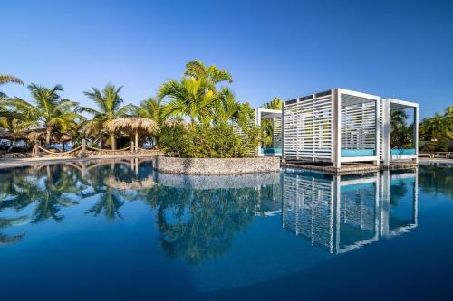 a swimming pool with blue water and palm trees at Delfins Beach Resort Bonaire, Tapestry Collection by Hilton in Kralendijk