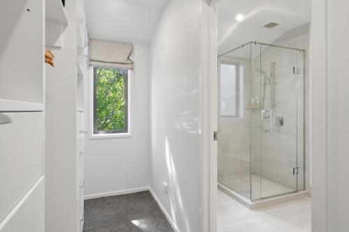 a white bathroom with a shower and a glass door at Rolki House - Hanmer Springs Holiday Home in Hanmer Springs
