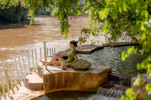 a woman sitting on a rock next to a river at Hintok River Camp in Sai Yok