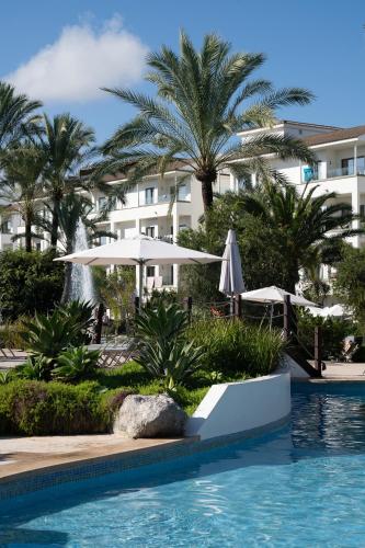 a pool at a resort with umbrellas and palm trees at Prinsotel La Dorada & Spa in Playa de Muro