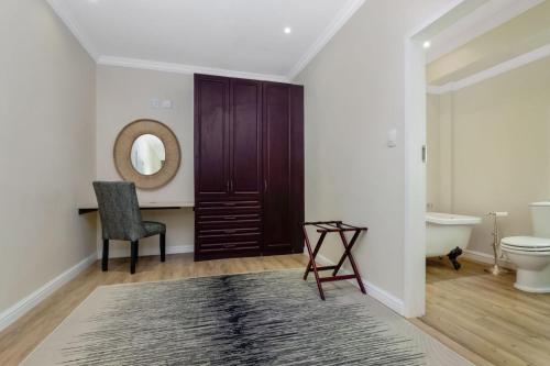 a bathroom with a toilet and a chair and a mirror at Manor On Main in Midrand