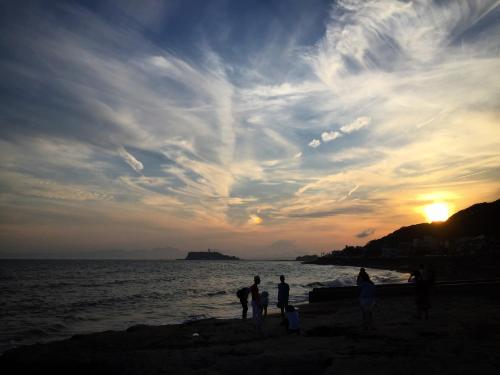 a group of people standing on the beach at sunset at IZA Kamakura Guest House and Bar in Kamakura