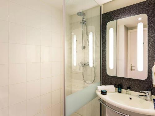a white bathroom with a sink and a mirror at Ibis Roscoff Bord de Mer in Roscoff