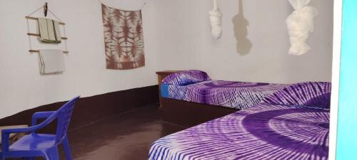 a bedroom with two purple beds and a blue chair at Campement Outouka in Kafountine