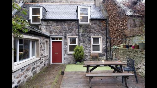 a picnic table in front of a stone building with a red door at Secret City Cottage - Peaceful - Private Garden in Aberdeen