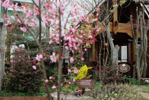 a tree with pink flowers in front of a house at Pension Yufuin in Yufuin