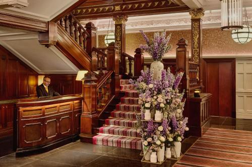 a man standing in a lobby with a staircase with flowers at The Connaught, Maybourne in London