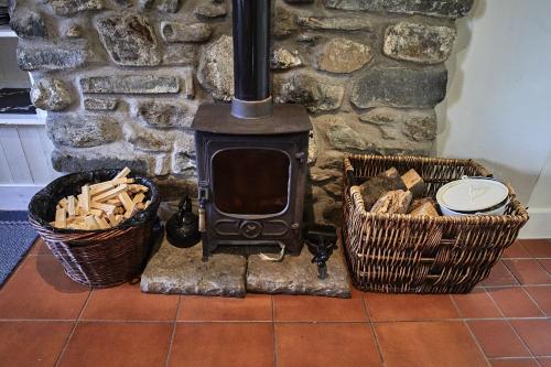 a stone fireplace with two baskets and a stove at Glenalbyn Cottage in Saint Fillans