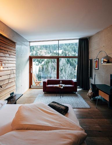 a bedroom with a bed and a couch and a large window at "Quality Hosts Arlberg" Hotel Lux Alpinae in Sankt Anton am Arlberg