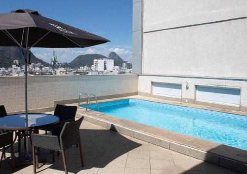 a patio with a table and an umbrella next to a pool at Riale Vilamar Copacabana in Rio de Janeiro