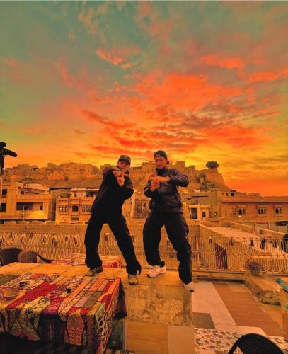 two men standing on a ledge in front of a sunset at Mirvana Guest House & Camel safari in Jaisalmer