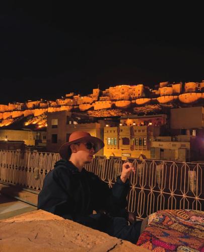 a man sitting on a ledge with a view of a city at Mirvana Guest House & Camel safari in Jaisalmer