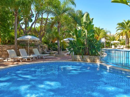 a swimming pool with chairs and umbrellas and palm trees at Ria Park Garden Hotel in Vale do Lobo