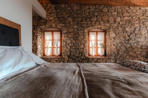 a stone walled bedroom with a bed and two windows at Vila Podigrac in Zgornja Kungota