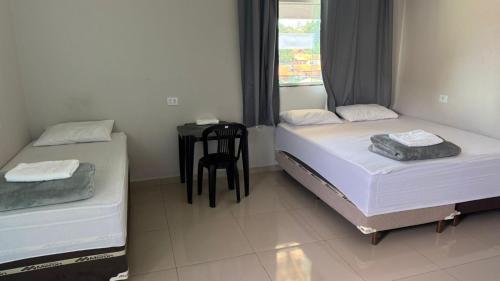 two beds in a room with a table and a chair at Hotel Serrinha in Botumirim