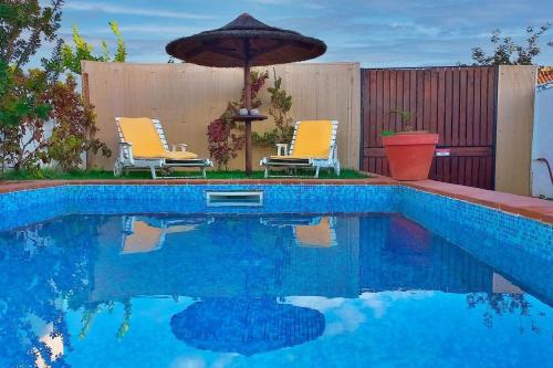 a swimming pool with two chairs and an umbrella at Vila Saraz Alqueva in Campinho