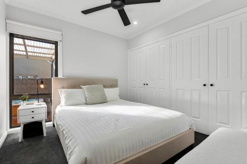 a white bedroom with a bed and a ceiling fan at Central Geelong Escape Spa, Fire Pit, Sleeps 10 in Geelong